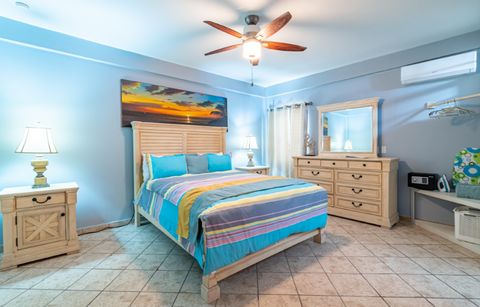 Deluxe Studio with a queen-size bed, bright striped bedspread, dresser with mirror and a ceiling fan